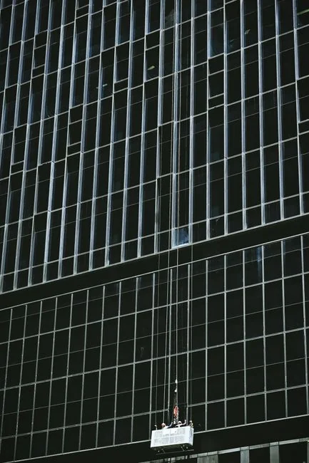 Two workers clean windows on a tall office building in a city setting.